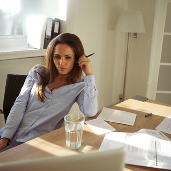 Woman in casual shirt working at home with laptop and documents.
