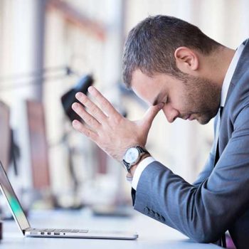 Stressed businessman with head in hands at his desk.