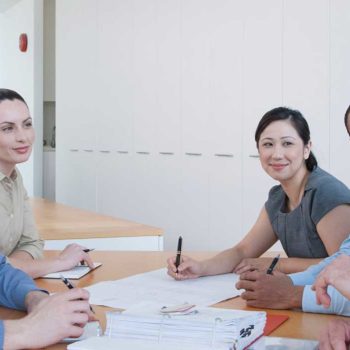 A diverse group collaborating at a meeting table with documents and pens.