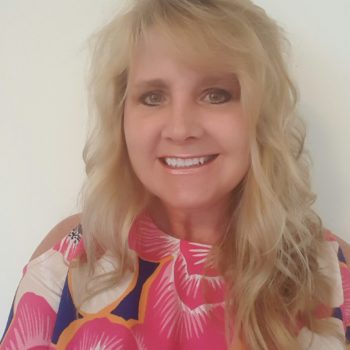Smiling woman with blonde hair and a colorful floral top.