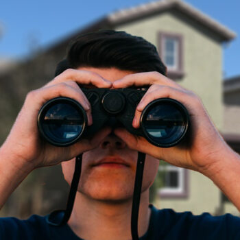 Person looking through binoculars near houses.