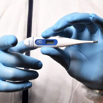 Gloved hands holding a digital thermometer.