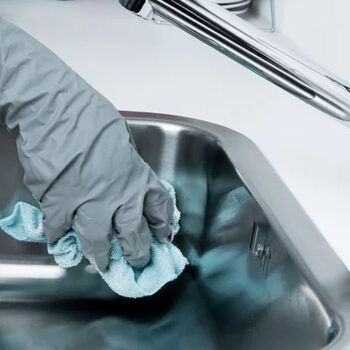 Gloved hand cleaning a stainless steel sink.