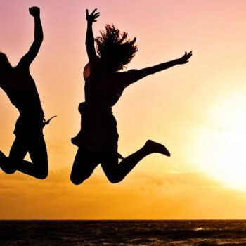 Two people jumping at sunset by ocean.