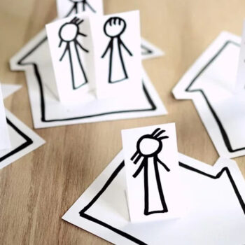Stick figures on paper houses, wooden background.
