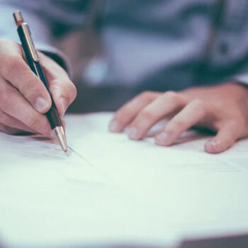 Person writing on paper with pen.