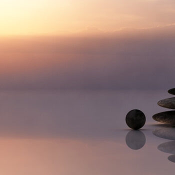 Stacked stones at sunrise over water.