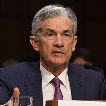 Man speaking at a conference, wearing a suit.